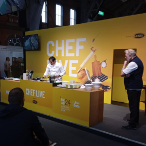 A chef presenting a live cooking demonstration at Northern Restaurant & Bar 2024's Chef Live stage, sponsored by UNOX
