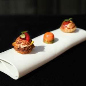 An elegant trio of gourmet bites presented on a sleek white platter, showcasing the artistry of MICHELIN Guide-inspired cuisine with vibrant, detailed garnishes