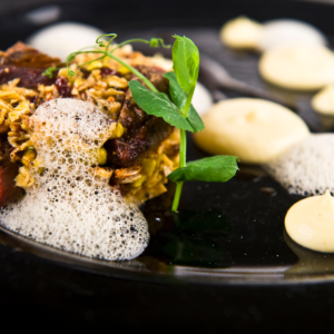 A MICHELIN Guide-worthy main course, featuring tender meat with a crunchy crust, artfully placed foam, and creamy dollops, garnished with fresh pea shoots for a refined touch